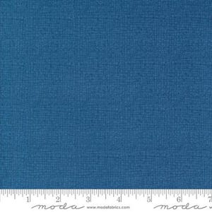 May include: A close-up of a textured, solid blue fabric. The fabric has a subtle grid pattern, and a ruler is at the bottom. The fabric is a deep shade of blue, and the texture gives it a slightly rough appearance. The fabric is likely used for quilting or sewing projects.