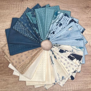 May include: A collection of fabric squares arranged in a circular pattern, showcasing various shades of blue and cream. The fabrics feature diverse patterns, including maps, dots, and geometric designs. A wooden button is at the center, holding the fabric together.