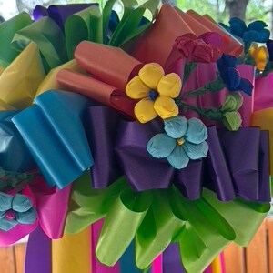Op de afbeelding: Een kleurrijk papieren bloemenarrangement met fel roze, blauwe, groene, gele en paarse linten. De bloemen zijn van papier en hebben een 3D-effect.