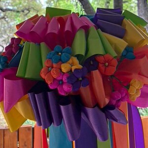 Op de afbeelding: Een kleurrijk papieren bloemenarrangement met roze, paarse, groene, gele en oranje papieren bloemen. De bloemen zijn in een cluster gerangschikt en hangen aan een plafond.