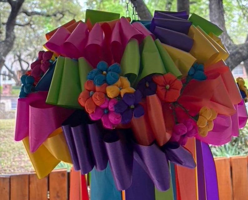 Op de afbeelding: Een kleurrijk papieren bloemenarrangement met roze, paarse, groene, gele en oranje papieren bloemen. De bloemen zijn in een cluster gerangschikt en hangen aan een plafond.