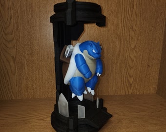 May include: A blue and white Pokemon figurine is displayed in a black 3D printed stand. The stand has a geometric design with a raised platform and a base with spikes.