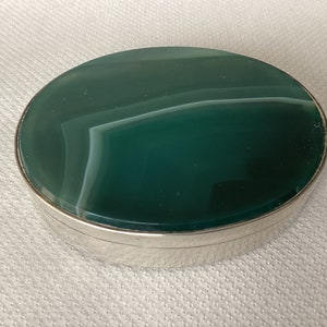 Puede incluir: Caja de alhajas ovalada con borde plateado y tapa de piedra de ágata verde.