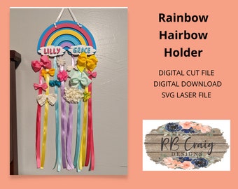 May include: A rainbow-coloured wooden hairbow holder with the names "Lilly" and "Grace" on it. The holder has ribbons in various colours hanging from it, and there are hairbows on the ribbons. The holder is a digital cut file for crafting.