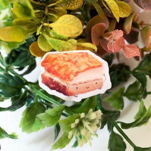 Könnte beinhalten: Ein Aufkleber mit einer Cartoon-Illustration eines Stücks knusprigen Schweinebauchs. Der Schweinebauch hat eine goldbraune, knusprige obere Schicht, eine weiße Mittelschicht und eine dunkelbraune untere Schicht. Der Aufkleber hat einen weißen Rand.