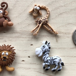 May include: Four plastic animal figurines: a brown monkey, a tan giraffe, a brown lion, and a black and white zebra. The figurines are about the size of a US quarter.