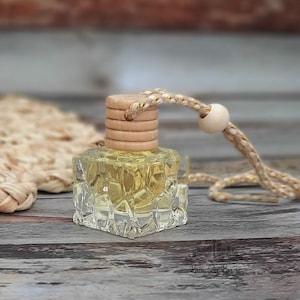 May include: A clear glass bottle with a textured surface filled with a light yellow liquid. The bottle has a wooden cap and a beige string with a wooden bead.