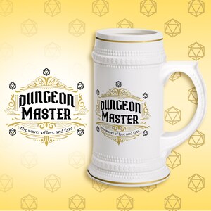 May include: A white ceramic beer stein featuring a black and gold graphic design. The text reads "DUNGEON MASTER" in a bold font, with "the waver of lore and fate" underneath. The design includes gold filigree and small black dice icons.