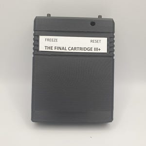 May include: A dark gray rectangular cartridge with the text "FREEZE" and "RESET" above "THE FINAL CARTRIDGE III+". The cartridge has a ridged design on the sides and two small protrusions on the top.