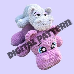 May include: Two crocheted stuffed hippos, one gray and one purple, with large eyes and a playful expression. The gray hippo is sitting on top of the purple hippo.