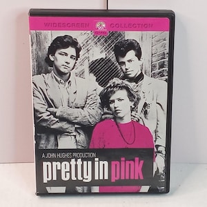 May include: A DVD case for the movie "Pretty in Pink" featuring a cast photo in black and white. The title is in pink, with a pink border at the top. The case is black.
