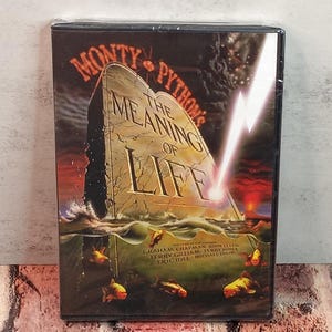 May include: A DVD of "Monty Python's The Meaning of Life" in a plastic case. The cover features a tombstone with the title, a lightning bolt, and fish. The film's cast and crew are listed at the bottom.