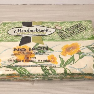 May include: A packaged, full-fitted Meadowbrook sheet set. The sheets are cream-colored with a floral pattern of yellow flowers and green leaves. The packaging includes text that reads "No Iron" and "For 54 x 75 in. Mattress".
