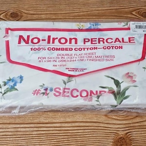 May include: A white double flat sheet in plastic packaging with a floral pattern. The label reads No-Iron PERCALE 100% COMBED COTTON, DOUBLE FLAT SHEET FOR 54x76 IN. MATTRESS, 81x96 IN. FINISHED SIZE, 200 THREAD COUNT, MADE IN U.S.A., and #1 SECONDS.