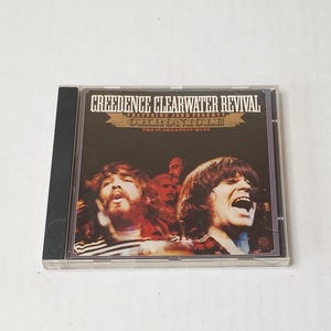 May include: A Creedence Clearwater Revival Chronicle The 20 Greatest Hits music CD in a clear plastic jewel case. The cover features a dark, vintage-style photograph of the band members performing, with white and gold text printed at the top.