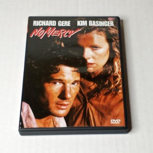 May include: A rectangular DVD case for the film No Mercy, featuring a dark, moody cover with portraits of actors Richard Gere and Kim Basinger. The title No Mercy is printed in a stylized red font at the top, with the DVD logo in the bottom corner.