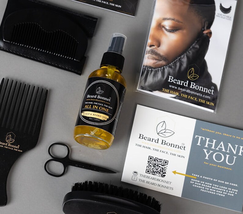 Pode incluir: Um gorro de barba preto, um pente preto, um par de tesouras pretas, uma escova de barba preta e uma garrafa de vidro transparente com um r&oacute;tulo preto que diz "Beard Bonnet All in One Scalp & Beard Oil" sobre uma superf&iacute;cie branca. O r&oacute;tulo tamb&eacute;m inclui o texto "www.beardbonnets.com The Hair. The Face. The Skin."