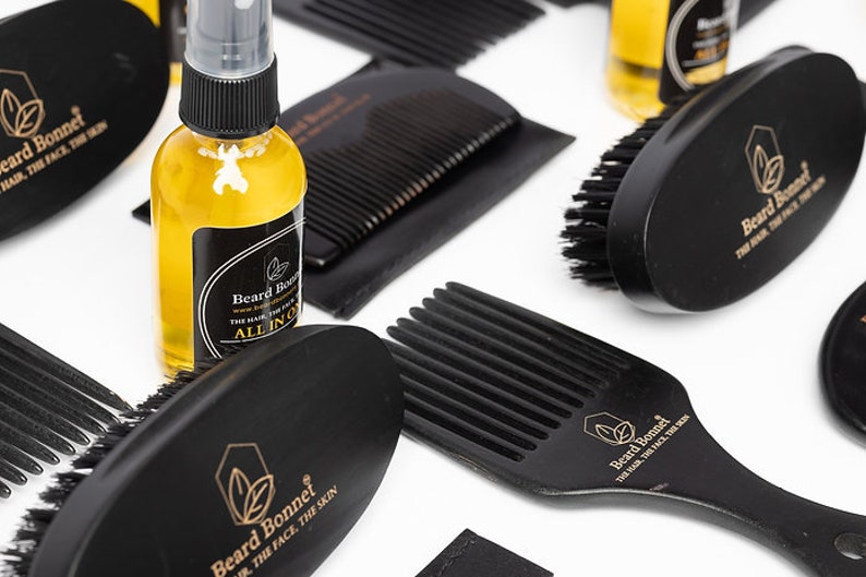 Pode incluir: Um conjunto de produtos para o cuidado da barba que inclui um pente de madeira preto, uma escova preta, um pente preto com cabo e uma garrafa de vidro transparente com tampa preta e um r&oacute;tulo dourado que diz "Beard Bonnet".