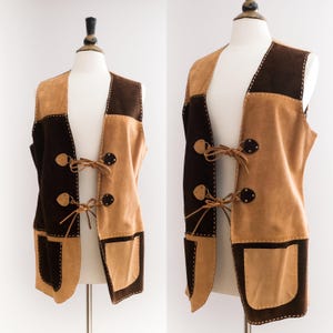 May include: A brown and tan suede waistcoat with a patchwork design. The waistcoat has a V-neck and a tie closure at the front.