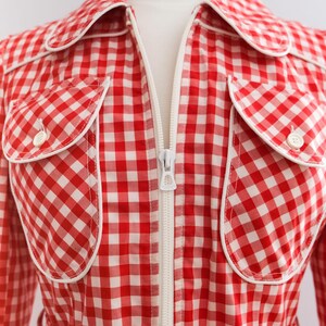 May include: Red and white gingham dress with a white zipper down the front and white piping around the collar and pockets. The dress has a belt.