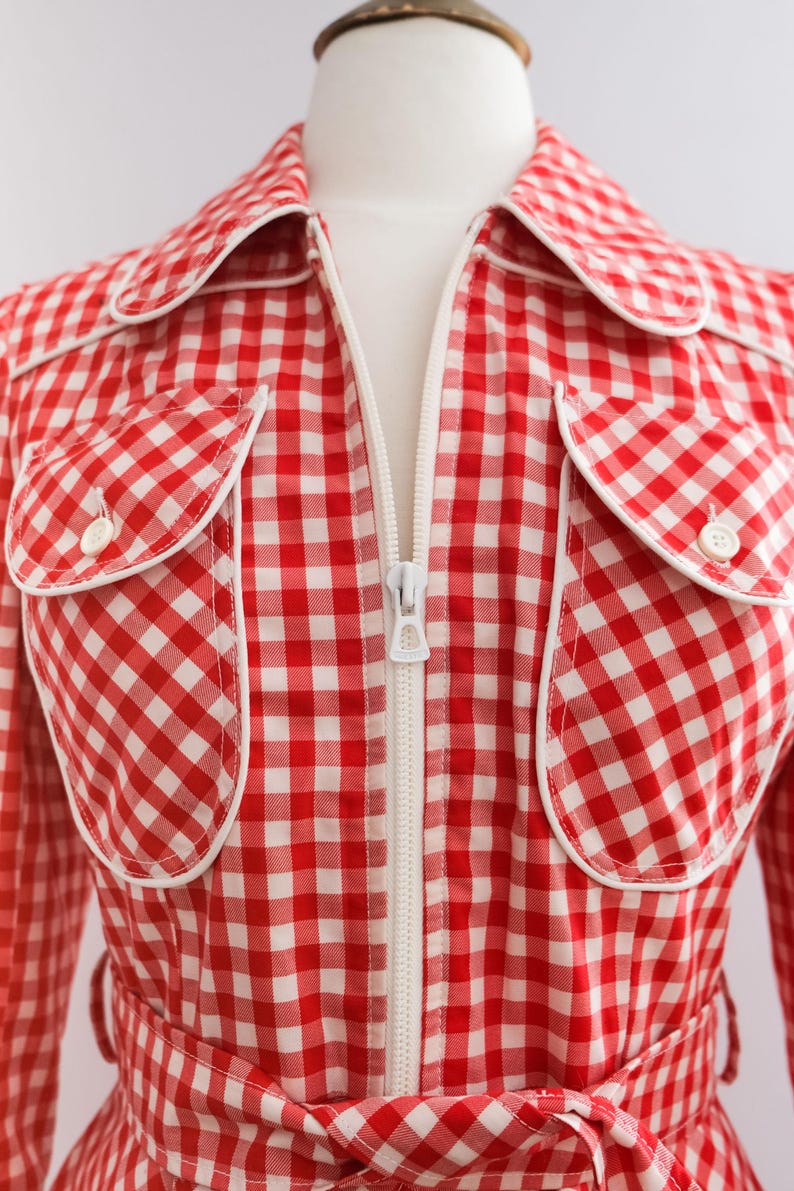 May include: Red and white gingham dress with a white zipper down the front and white piping around the collar and pockets. The dress has a belt.