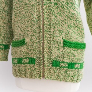 May include: A vintage green and cream-colored knitted cardigan with a full zipper closure. The sweater features two front pockets and green trim details. The knitwear has a chunky texture.