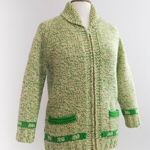 May include: A vintage green and cream-colored knitted cardigan with a full zipper closure. The sweater features two front pockets and green trim on the cuffs and bottom hem. The cardigan is displayed on a mannequin.