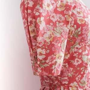 May include: A floral print dress in shades of red, pink, and white. The dress features short sleeves with buttoned cuffs and a fitted bodice. The fabric has a delicate floral pattern.