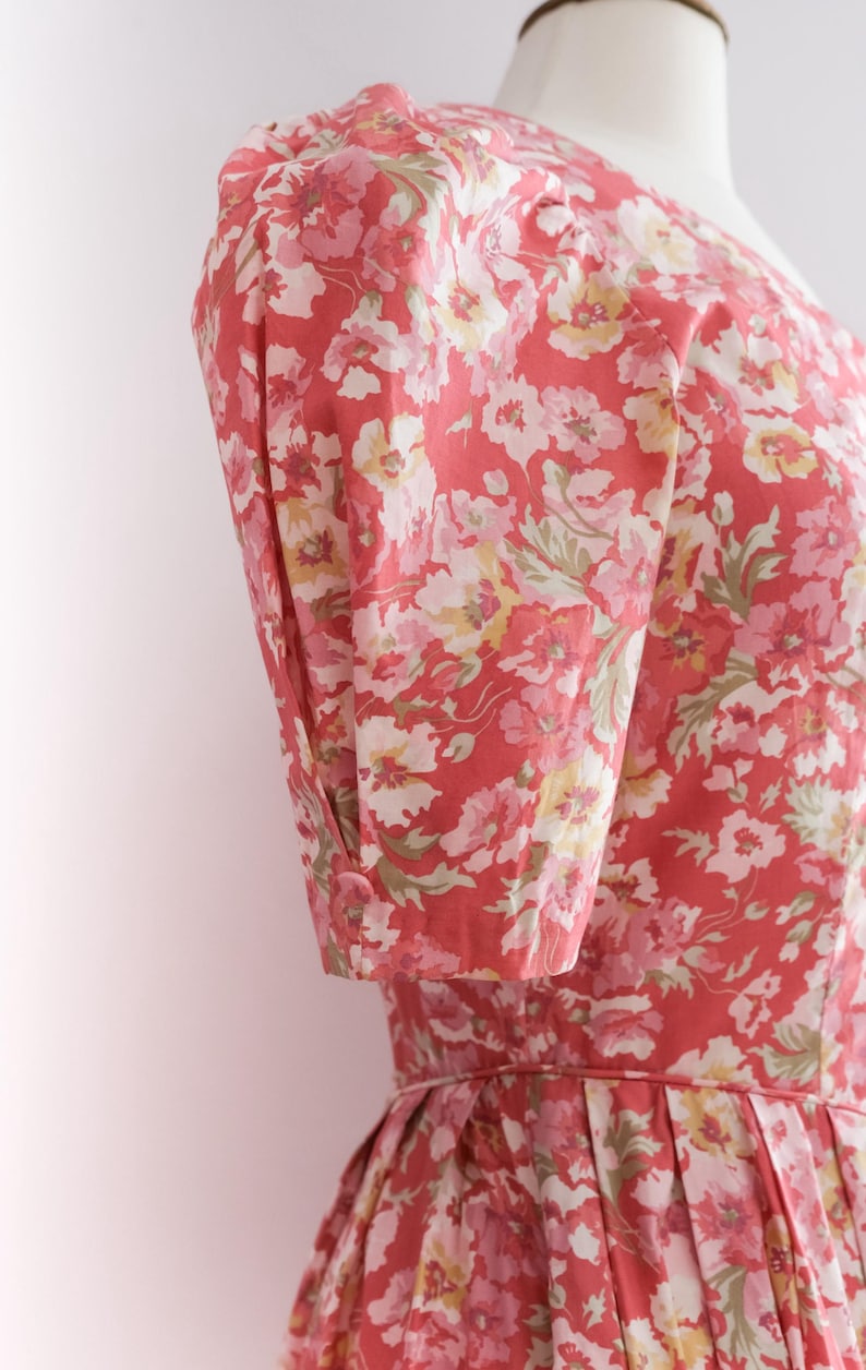 May include: A floral print dress in shades of red, pink, and white. The dress features short sleeves with buttoned cuffs and a fitted bodice. The fabric has a delicate floral pattern.