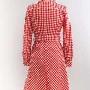 May include: Red and white gingham dress with a white trim and a belt. The dress has long sleeves and a flared skirt.