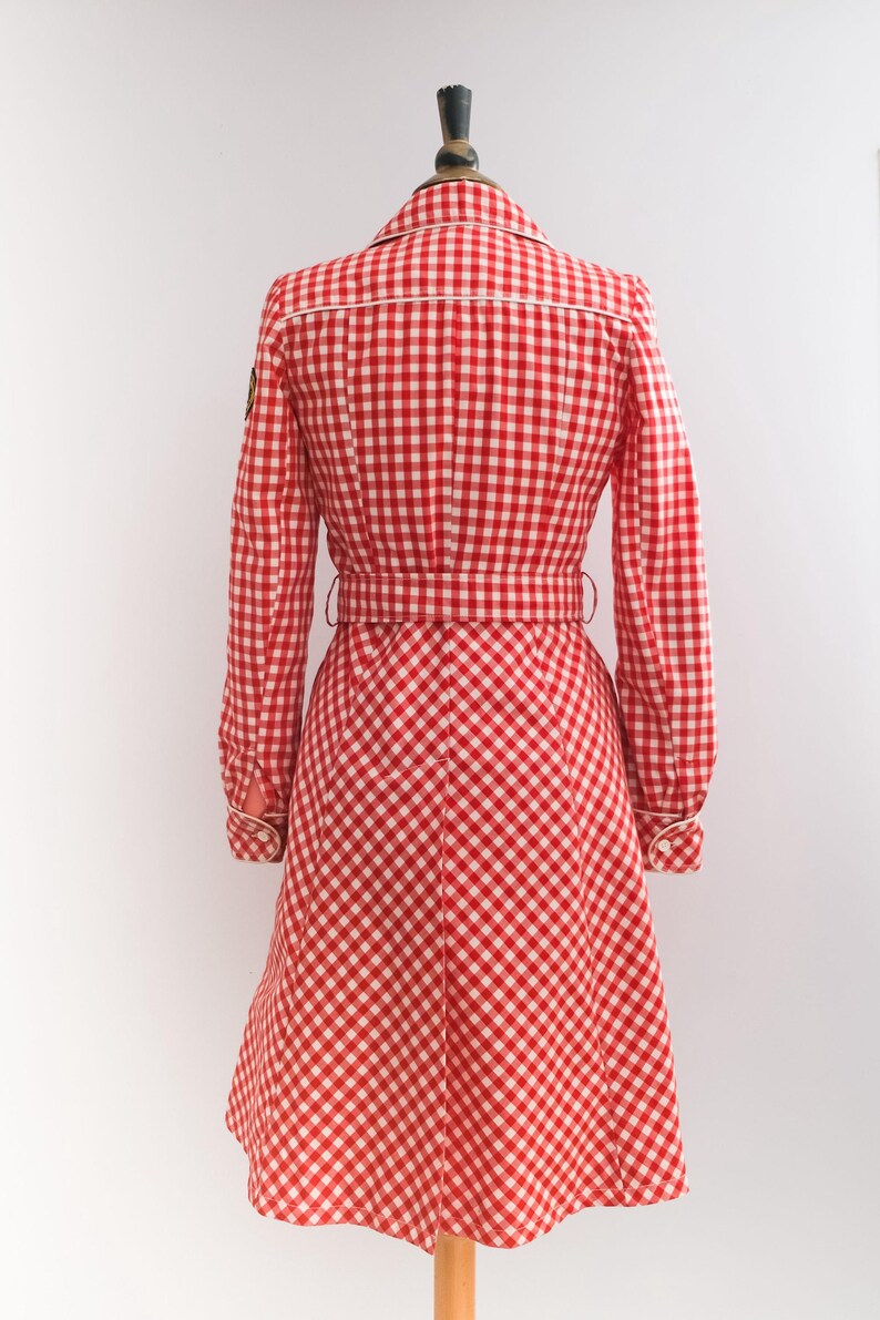 May include: Red and white gingham dress with a white trim and a belt. The dress has long sleeves and a flared skirt.