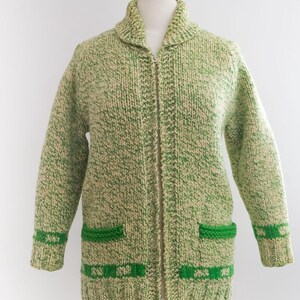 May include: A vintage green and cream-colored knit cardigan with a zipper closure. The sweater features two front pockets and green detailing on the cuffs and pockets. The collar is a shawl style.