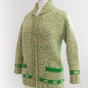 May include: A green and cream-colored knitted cardigan with a collared neckline and a full zipper. The sweater features green accents on the pockets and cuffs. The cardigan is displayed on a mannequin.