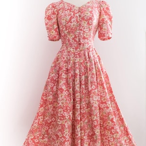 May include: A vintage-style, floral-print dress in shades of red, pink, and white. The dress features a V-neckline, short puffed sleeves, and a button-down bodice. The skirt is a full, flowing A-line, perfect for a retro look.