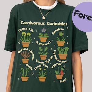 May include: Dark green t-shirt featuring the text "Carnivorous Curiosities" and illustrations of various carnivorous plants, including Cobra Lily, Sundew, and Venus flytrap. A purple circle with the word "Forest" is in the upper right corner.