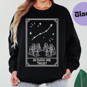 Puede incluir: Sudadera negra con un gráfico blanco. El gráfico presenta una constelación con una flecha hacia arriba, estrellas y el texto "IN DATA WE TRUST". La sudadera es de estilo casual.