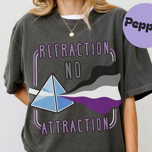 May include: Dark gray t-shirt with the text "REFRACTION NO ATTRACTION" in purple and white. A prism graphic refracts light into the asexual pride flag colors. A purple circle with the word "Pepper" is in the upper right.