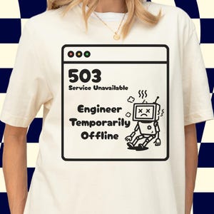 May include: A cream-coloured t-shirt with a black and white graphic depicting a computer error message. The message reads "503 Service Unavailable Engineer Temporarily Offline" with a sad robot illustration. The shirt has short sleeves.