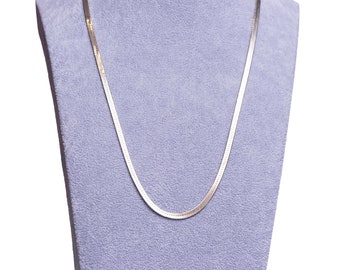 Puede incluir: Un collar de cadena de plata en un expositor de terciopelo morado.
