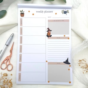 Könnte beinhalten: Ein weißer Wochenplaner-Block mit der Aufschrift weekly planner oben. Das Layout enthält tägliche Abschnitte von Montag bis Sonntag, einen Dankbarkeitsbereich mit einer kleinen Hexenillustration, eine Aufgabenliste und einen Notizbereich.