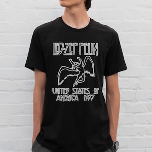 K&ouml;nnte beinhalten: Schwarzes T-Shirt mit einer wei&szlig;en Grafik einer gefl&uuml;gelten Figur und dem Text "LED-ZEP PELIN UNITED STATES of AMERICA 1977".