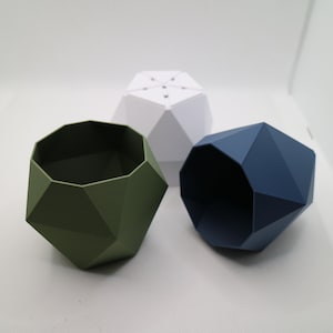 May include: Three geometric planters in different colors: green, white, and blue. The planters are made of a smooth, textured material and have a unique, modern design.