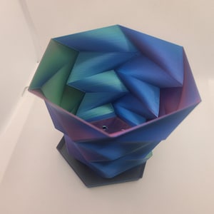 May include: A geometric planter with a blue, green and purple iridescent finish. The planter has a hexagonal base and a unique, folded design.