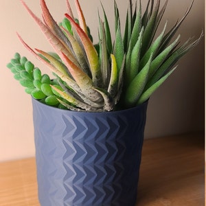 Puede incluir: Una maceta azul con un patrón texturizado contiene una variedad de suculentas verdes y rojas.