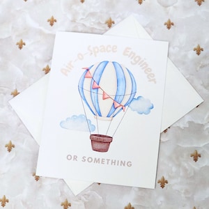 May include: A white card with a blue and white striped hot air balloon with pink flags. The text "Air-o-Space Engineer or Something" is written on the card.