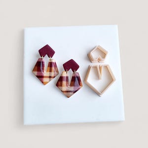 May include: A pair of plaid earrings with a burgundy top and a geometric shape. The earrings are in a plaid pattern of burgundy, tan, and brown. Two earring cutters are also in the image.