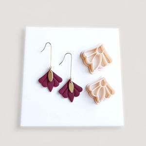 May include: A pair of burgundy leather earrings with gold-colored accents and matching polymer clay earring cutters. The earrings have a fan-like design and are displayed on a white surface.