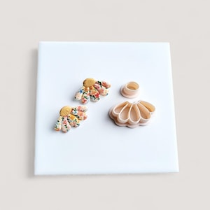 May include: Two floral daisy earrings with yellow centres and a matching set of polymer clay cutters. The cutters include a daisy shape and a small cylinder. The earrings feature a colourful floral pattern.