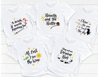 May include: Five white t-shirts with different Disney-themed designs. The shirts feature text and images from the movies Tangled, Beauty and the Beast, and Peter Pan. The text on the shirts includes phrases like "A drink worth fighting for", "Beauty and the Bottle", "Chase the wine and touch the sky", "At Last I see the Wine", and "They call me Drinker Bell".