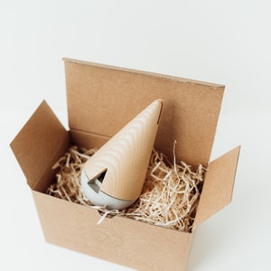 May include: A wooden and gray cone-shaped incense burner sits in a brown cardboard box filled with shredded paper. The box has a logo with two mountains and the word "Mountain" printed on it.